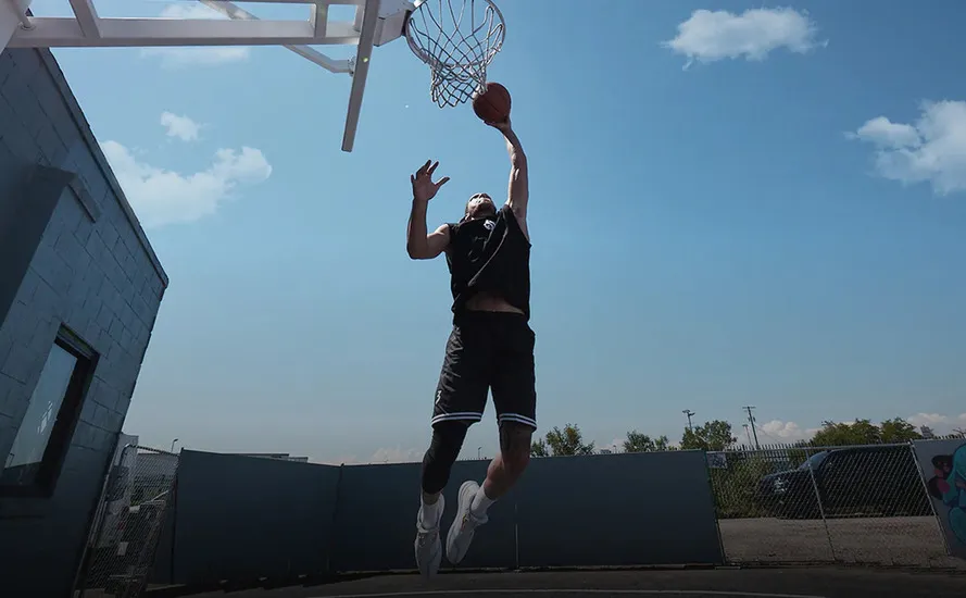 Баскетболист в кроссовках бренда 361° на уличной площадке полпрыгивает, чтобы забить мяч в кольцо