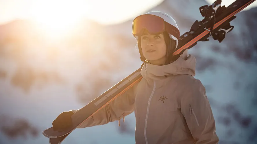 Девушка в экипировке и с лыжами компании ATOMIC.