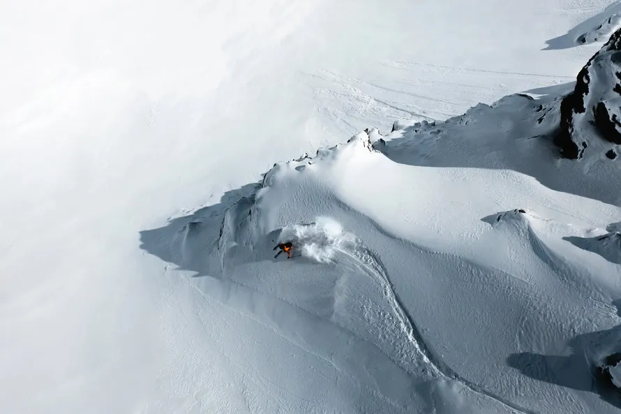 Ски-альпинист спускается с гор на лыжах и в экипировке компании ATOMIC. Вид сверху.