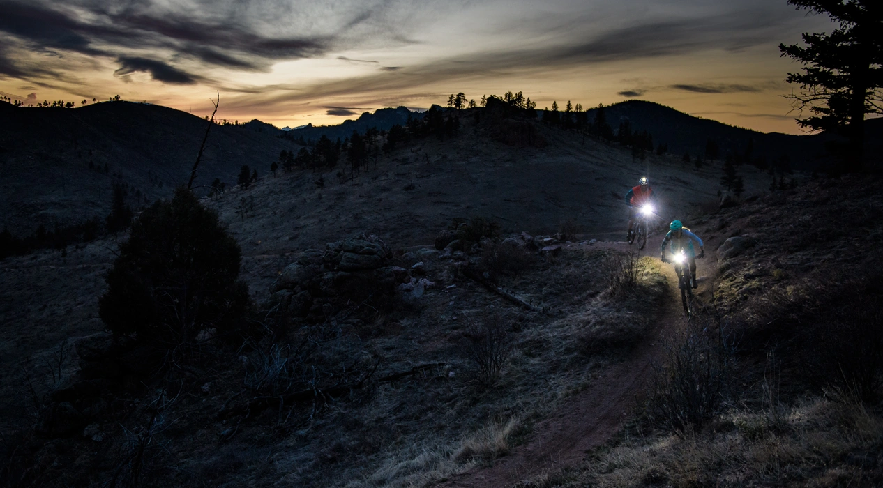 два велосипедиста спускаются с горы в сумерках с фонарями