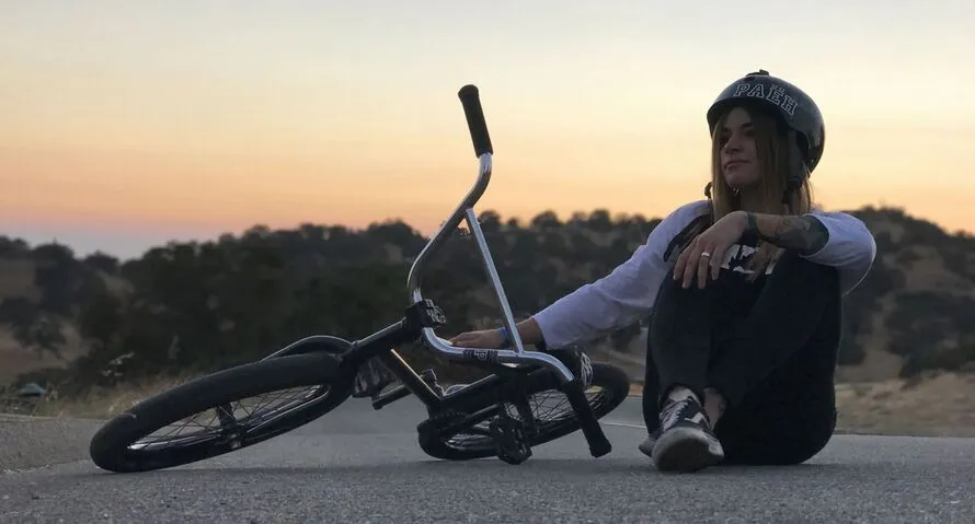 Девушка сидит на земле рядом с велосипедом BMX производства компании KHEBIKES.