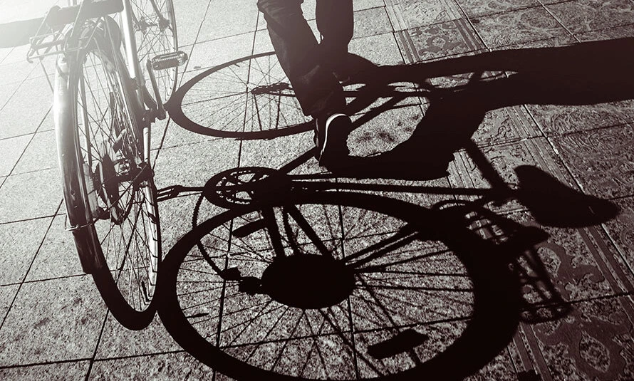 Тень на тротураной плитке от мужчины, идущего с велосипедом.