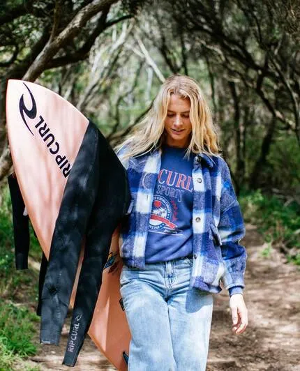 Девушка в экипировке Rip Curl и с доской для сёрфинга производства Rip Curl..