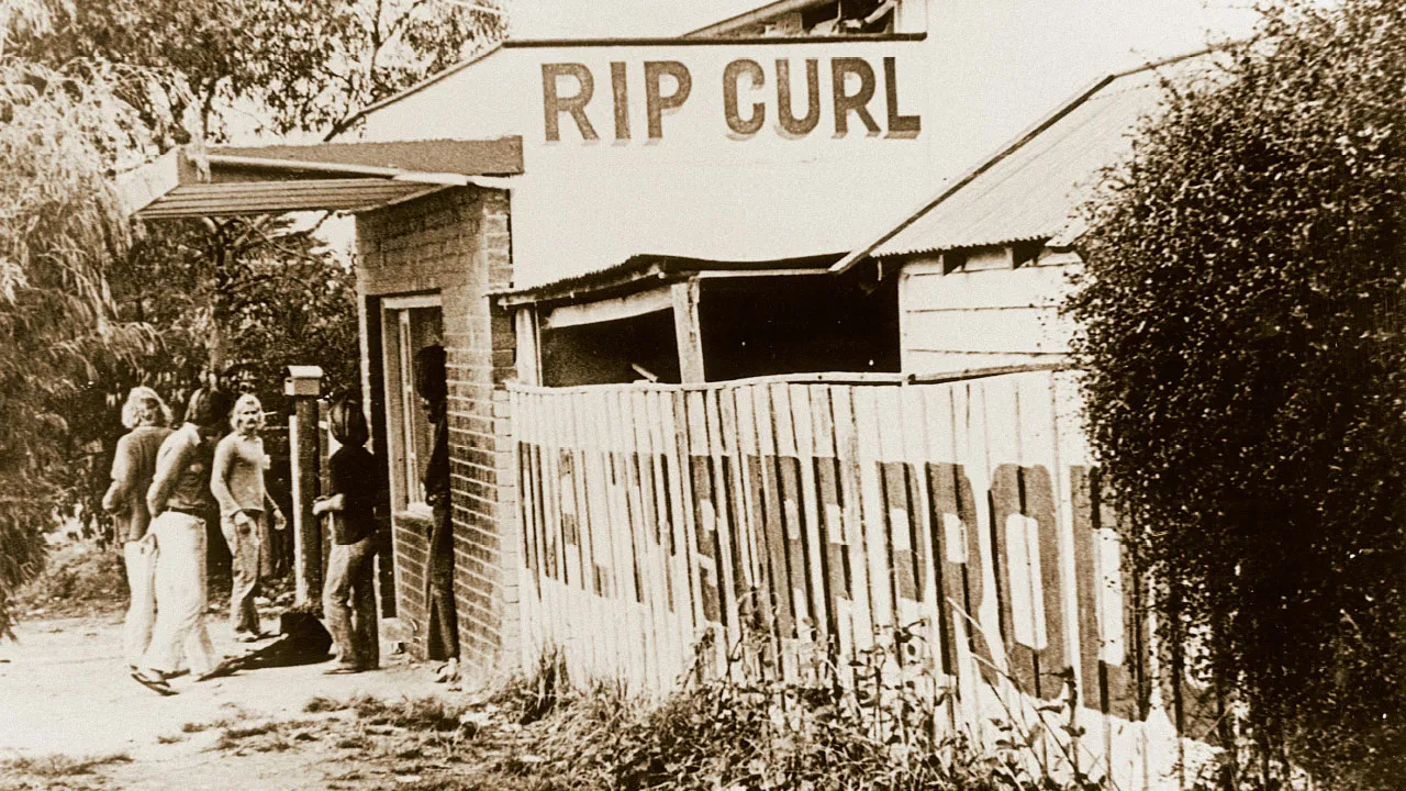 Снимок старой пекарни в оттенках сепии, самой первой модернизации завода Rip Curl, с четырьмя мужчинами, стоящими у входа.