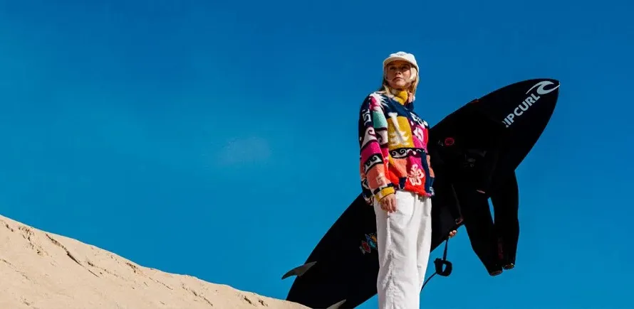 Девушка в джакете Rip Curl держит доску для серфинга компании Rip Curl.