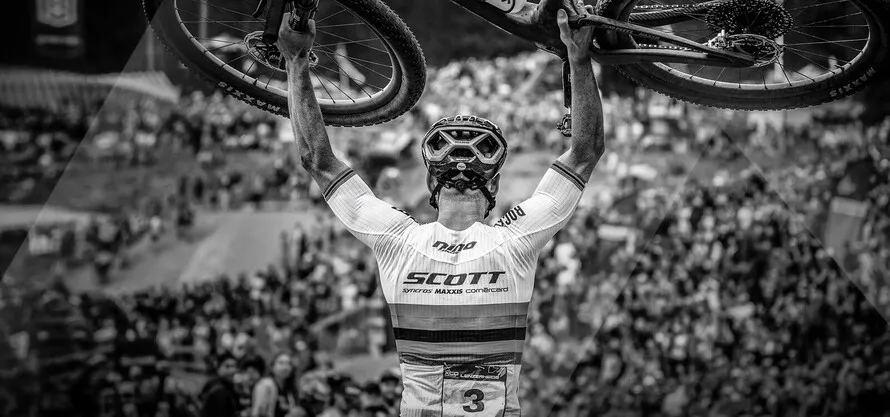 Спортсмен с поднятым вверх на руках велосипедом компании SCOTT.