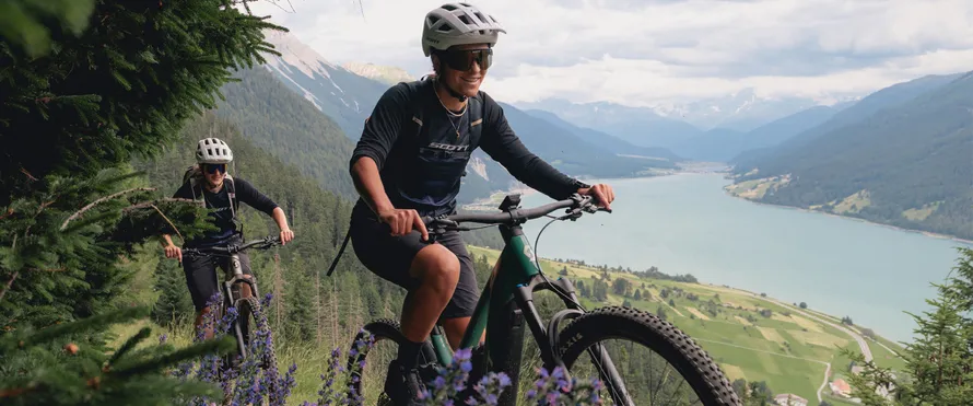 Девушка и парень едут по лесной тропе в экипировке и на велосипедах компании SCOTT.