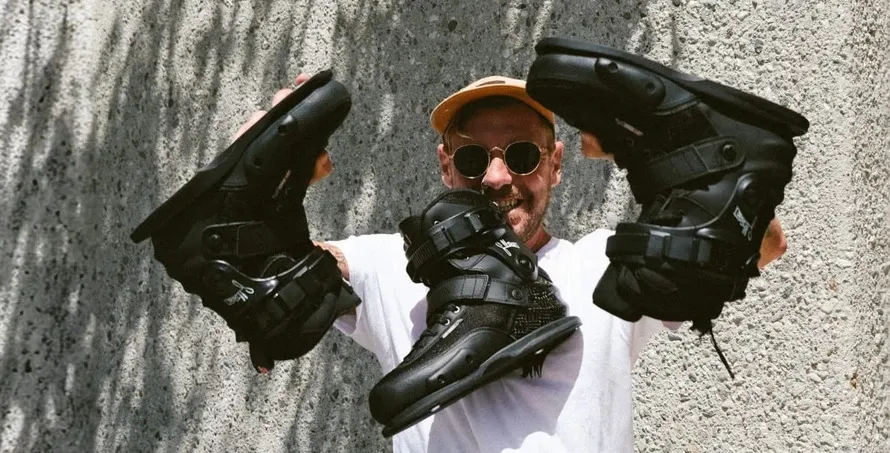 Мужчина в очках держит три ботинка SEBA CJ2 BlackSEBA для уличного катания производства компании SEBA.