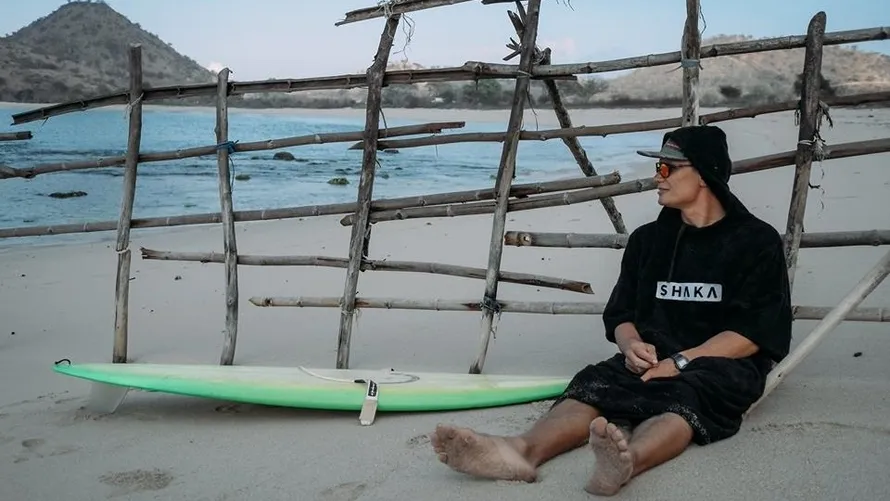 Девушка сидит на пляже в худи лонг производства бренда SHAKA.