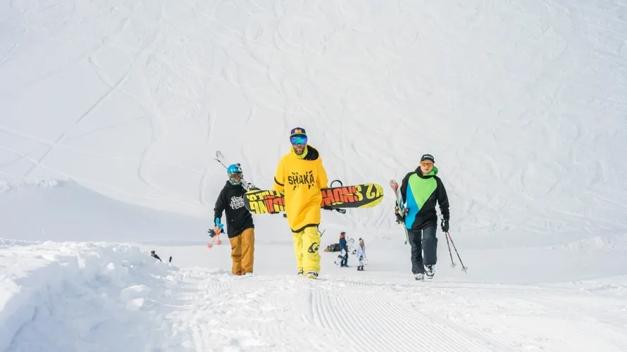 Трое мужчин поднимаются по снежному склону в одежде бренда SHAKA.