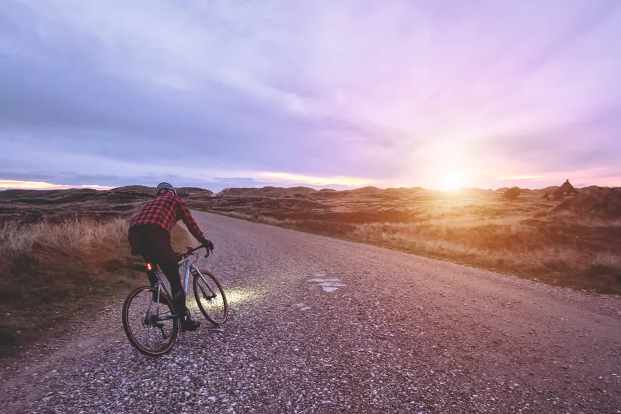 Велосипедист едет по проселочной дороге на велосипеде с устанвленным на нем задним велофонарем производства компании SIGMA.