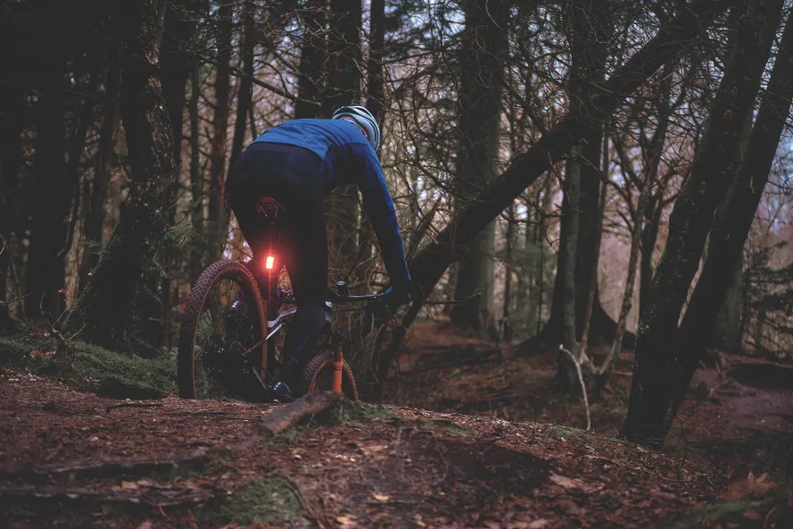 Мужчина едет по лесной тропинке на велосипеде с установленным задним фонарем производства компании SIGMA.