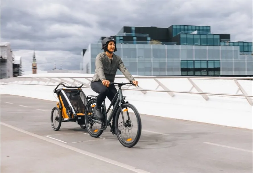 Девушка едет по городу на велосипеде с прицепом компании THULE.